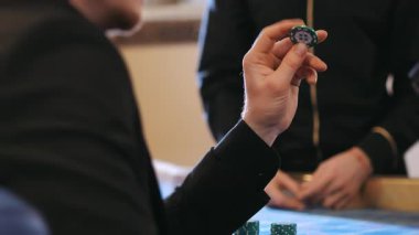 Çipi döndüren takım elbiseli bir adamın eli. Kumarhanede adamın biri elinde çip tutuyor. Kumarhanede poker oynayan bir adam..