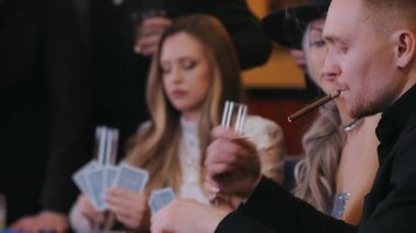 Takım elbiseli bir adam puro yakıyor ve kumarhanede poker oynarken sigara içmeye başlıyor. Bir adam kumarhanede puro içiyor. Kumarhane kavramı.