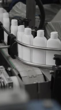 Kozmetik ürünleri için beyaz plastik şişeler bir fabrikada taşıyıcı bant boyunca hareket eder. Şampuan, duş jeli ve sıvı sabun üretimi. Kozmetik üretim tesisi. Dikey video