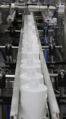 Kozmetik fabrikasında çalışan bir işçi boş plastik şişeleri taşıyıcıya yerleştirir. Plastik şişe üretim tesisi. Beyaz boş plastik şişeler bir fabrikada taşıyıcı boyunca hareket eder. Dikey video
