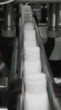 Kozmetik üretim tesisi. Kapakları şişelere vidalayan mekanizmaya yakın çekim. Şampuan üretimi, duş jelleri ve sıvı sabun. Dikey video.