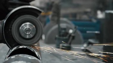 Metal fabrikasında çalışan bir işçi metali işliyor. Öğütücüden kıvılcımlar çıkıyor. Metal üretim fabrikası.