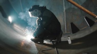 Koruyucu maskeli profesyonel bir kaynakçı büyük bir tankın içinde çalışır. Metal bir inşaat fabrikası. Kocaman bir silindirde kaynak izleri var. Endüstriyel ısıtma kazanı üretimi. c Fabrikası.