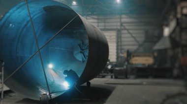 Koruyucu maskeli profesyonel bir kaynakçı büyük bir tankın içinde çalışır. Metal bir inşaat fabrikası. Kocaman bir silindirde kaynak izleri var. Endüstriyel ısıtma kazanı üretimi. c Fabrikası.
