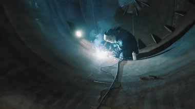 Koruyucu maskeli profesyonel bir kaynakçı büyük bir tankın içinde çalışır. Metal bir inşaat fabrikası. Kocaman bir silindirde kaynak izleri var. Endüstriyel ısıtma kazanı üretimi. c Fabrikası.