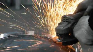 Metal fabrikasında çalışan bir işçi metali işliyor. Öğütücüden kıvılcımlar çıkıyor. Metal üretim fabrikası.