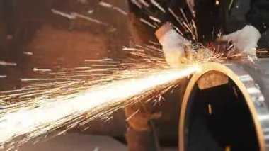 Metal fabrikasında çalışan bir işçi metali işliyor. Öğütücüden kıvılcımlar çıkıyor. Metal üretim fabrikası.