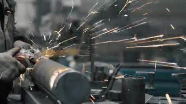 Metal fabrikasında çalışan bir işçi metali işliyor. Öğütücüden kıvılcımlar çıkıyor. Metal üretim fabrikası.