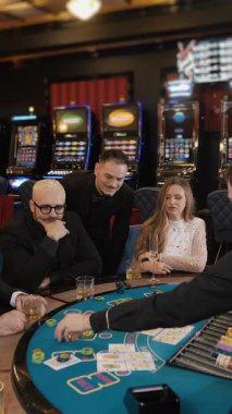 Erkekler ve kadınlar kumarhanede oynamak için masada oturuyorlar. Kumarhanede oyun masasında oynayan bir grup insan. Kumar konsepti. Dikey video.