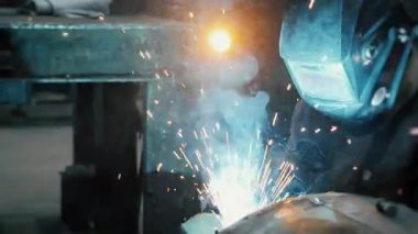  Koruyucu maskeli bir fabrikada çalışan bir işçi metal bir yapıyı kaynaklıyor. Metal yapılar üreten bir fabrika. Kaynak metalinden kıvılcımlar. Endüstriyel üretim. 