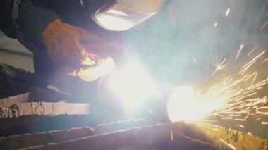 Bir fabrikada koruyucu maske takan bir işçi, elle tutulan bir plazma kesiciyle demir bir boruda delik açıyor. Metal yapılar ve ısıtma kazanları üretimi için endüstriyel fabrika.