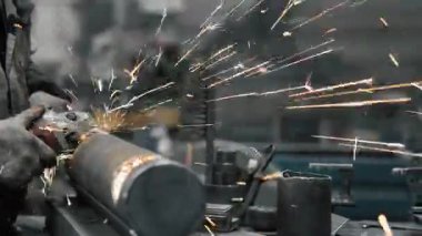 Metal fabrikasında çalışan bir işçi metali işliyor. Öğütücüden kıvılcımlar çıkıyor. Metal üretim fabrikası.