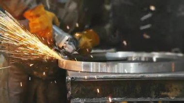 Bir işçi metal fabrikasında öğütücüyle çelik bir çember öğütüyor. Sıcak metalden kıvılcımlar çıkıyor. Adam fabrikada çeliğin üzerinde çok çalıştı.. 