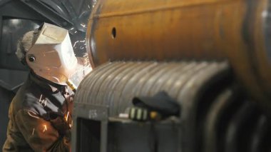 Koruyucu maskeli bir fabrikada çalışan bir işçi metal bir yapıyı kaynaklıyor. Metal yapılar üreten bir fabrika. Kaynak metalinden kıvılcımlar. Endüstriyel üretim. 