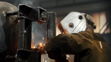 Koruyucu maskeli bir fabrikada çalışan bir işçi metal bir yapıyı kaynaklıyor. Metal yapılar üreten bir fabrika. Kaynak metalinden kıvılcımlar. Endüstriyel üretim. 
