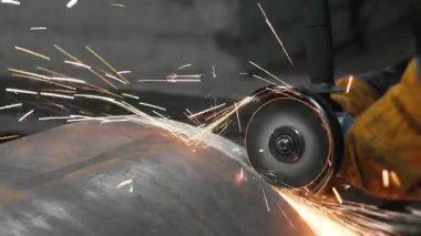 Metal fabrikasında çalışan bir işçi büyük bir boruyu öğütücüyle işliyor. Metal kıvılcımları ağır sanayi fabrikasında üretiliyor. Metal öğütme işlemi. Çelik fabrikası..