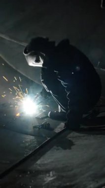 Koruyucu maskeli profesyonel bir kaynakçı büyük bir tankın içinde çalışır. Metal bir inşaat fabrikası. Kocaman bir silindirde kaynak izleri var. Endüstriyel ısıtma kazanı üretimi. Dikey video.