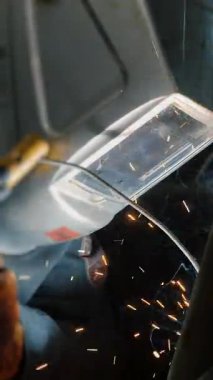  Koruyucu maskeli bir fabrikada çalışan bir işçi metal bir yapıyı kaynaklıyor. Metal yapılar üreten bir fabrika. Kaynak metalinden kıvılcımlar. Endüstriyel üretim. Dikey video.