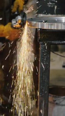 Metal fabrikasında çalışan bir işçi metali işliyor. Öğütücüden kıvılcımlar çıkıyor. Metal inşaat fabrikası. Dikey video.