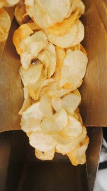 Kızarmış patates cipsi fabrikadaki endüstriyel taşıma bandına konuyor. Kızarmış cips yığını fabrikadaki bir konteynırda son buluyor. Chips Fabrikası. Dikey video.