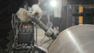 Fabrikadaki bir işçi büyük bir demir boruya elle vida takar. Endüstriyel metalcilik ve metal işleme.