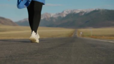 Dağlarda yol boyunca yürüyen bir kadının arka görüntüsü. Sırt çantasıyla yolda yürüyen bir kadın turist..