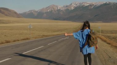 Dişi bir gezgin dağ yolunda otostop çekiyor ve yürüyor. Omuzlarında sırt çantası olan bir kız turist geçen arabalarla dağ yolunda yürüyor ve eliyle bir arabayı durdurmaya çalışıyor..