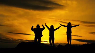 Üç turistin siluetleri gün batımının arka planında onların başarılarıyla sevinir ve elleri havada atlarlar..