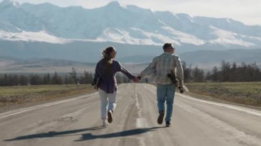 Bir çift genç turist, bir erkek ve bir kadın, dağ yolunda uzun tahta tutarak koşuyorlar. Dağlara aile gezisi..