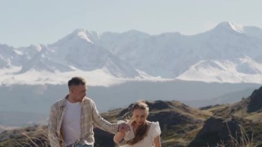 Birbirine aşık genç bir çift dağın tepesinde el ele yürüyor ve karla kaplı dağların güzel manzarasının tadını çıkarıyorlar..