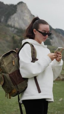Dişi bir turist, dağlarda telefonuyla seyrüsefer rotasına bakıyor. Turist dağlarda mobil bir ağ yakalamaya çalışıyor. Dikey video.