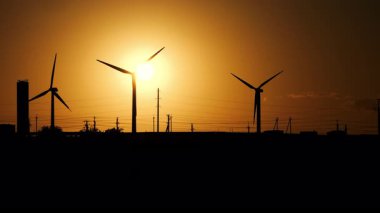 Rüzgar türbinlerinin siluetleri gün batımında bir tarlada elektrik üretiyor. Alternatif temiz enerji kaynakları rüzgara dayanıyor. Rüzgarın elektriğe dönüşümü.