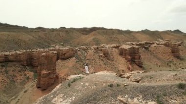 Beyaz elbiseli kadın turist, Red Rock Kanyonu 'nda uçurumun kenarında duruyor. İnanılmaz kırmızı kaya manzarasının tadını çıkarıyor. Panoramik drone manzarası..