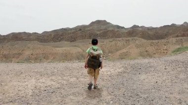 Şapkalı ve sırtında sırt çantası olan küçük bir çocuk dağın tepesindeki uçuruma doğru yürür ve kanyonun güzel manzarasına hayran kalır..