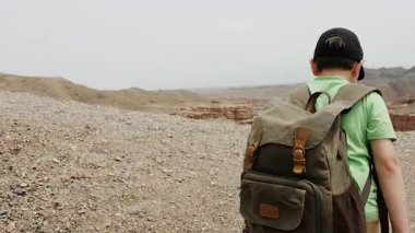 Şapkalı ve sırtında sırt çantası olan küçük bir çocuk dağın tepesindeki uçuruma doğru yürür ve kanyonun güzel manzarasına hayran kalır..
