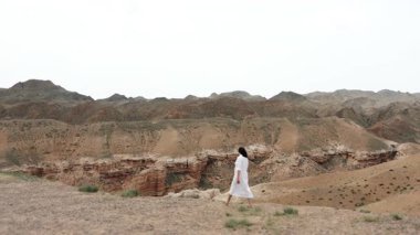 Beyaz elbiseli kadın turist Red Rock Kanyonu 'nda uçurumun kenarına yürüyor. İnanılmaz kırmızı kaya manzarasının tadını çıkarıyor..