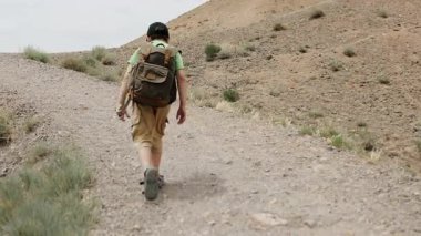 Şapkalı ve sırtında sırt çantası olan küçük bir çocuk dağın tepesindeki uçuruma doğru yürür ve kanyonun güzel manzarasına hayran kalır..