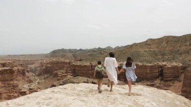 Bir grup turist, iki çocuklu bir anne, bir oğlan ve bir kız, bir uçurumun kenarına yaklaşıyorlar ve ulusal parktaki kanyonun güzel manzarasının tadını çıkarıyorlar.
