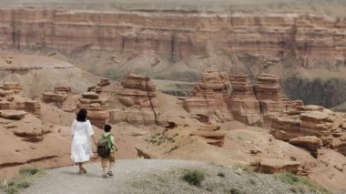 İki turist, sırtında sırt çantası olan küçük bir çocukla bir anne, bir uçurumun kenarında el ele yürürler ve ulusal parktaki güzel bir kanyonun manzarasının tadını çıkarırlar..