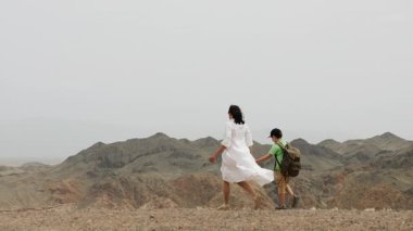 İki turist, sırtında sırt çantası olan küçük bir çocukla bir anne, bir uçurumun kenarında el ele yürürler ve ulusal parktaki güzel bir kanyonun manzarasının tadını çıkarırlar..