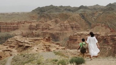 İki turist, sırtında sırt çantası olan küçük bir çocukla bir anne, bir uçurumun kenarında el ele yürürler ve ulusal parktaki güzel bir kanyonun manzarasının tadını çıkarırlar..