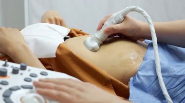 Modern tarayıcısı olan bir hastaya karın boşluğunun ultrasonunu yapan bir ultrason doktorunun ellerini yakın çekim. Bir üreme kliniğinde modern tıbbi teşhis ekipmanları.