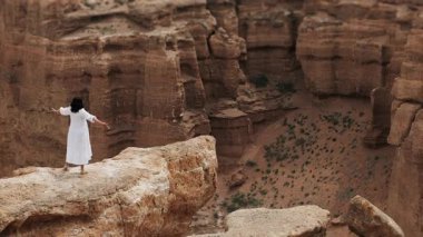 Beyaz elbiseli kadın turist Red Rock Kanyonu 'nda uçurumun kenarında duruyor. İnanılmaz kırmızı kaya manzarasının tadını çıkarıyor..