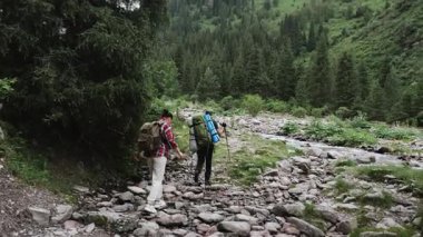 Omuzlarında sırt çantaları olan iki turist, bir adam ve bir kadın dağ nehri boyunca bir dağ yolu boyunca bir dağa tırmanıyorlar..