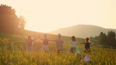Beş genç turistten oluşan bir grup gün batımında bir tarlada durup ellerini kaldırarak, dağlarda tatillerinin tadını çıkarıyorlar..