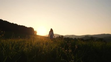 Gün batımında yeşil arazide koşan genç ve güzel bir turist kızı silueti..