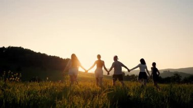 Bir grup insanın siluetleri yürür, ellerini kaldırır ve gün batımının arka planına karşı yaptıkları başarıya sevinirler..