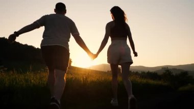 Gün batımında birbirine aşık genç bir çiftin siluetleri dağlarda bir tarlada el ele koşuşturuyor..