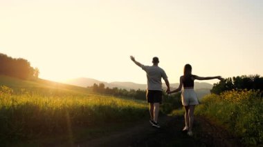 Birbirlerine aşık genç bir çiftin siluetleri gün batımında dağlarda bir köy yolunda yürüyorlar. Birbirlerinin ellerini tutuyorlar..