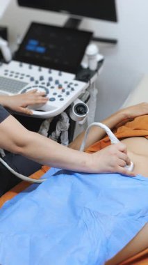 Modern tarayıcısı olan bir hastaya karın boşluğunun ultrasonunu yapan bir ultrason doktorunun ellerini yakın çekim. Modern tıbbi teşhis ekipmanları. Dikey video.